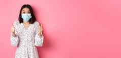 科维德检疫生活方式概念兴奋亚洲女人脸面具显示竖起大拇指赞扬好工作惊讶相机站粉红色的背景