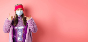 科维德社会距离时尚概念微笑亚洲高级女人时尚衣服呼吸器指出脸面具显示翘拇指粉红色的背景
