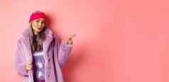 时尚的亚洲高级女人很酷的紫色的冬天外套指出手指显示广告时髦的相机粉红色的背景