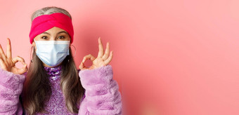 科维德病毒时尚概念特写镜头时尚亚洲高级女人脸面具显示迹象快乐粉红色的背景