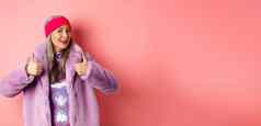时尚购物概念时尚的亚洲奶奶时尚的高级朝鲜文女人冬天人造革外套显示竖起大拇指批准赞扬好产品粉红色的背景