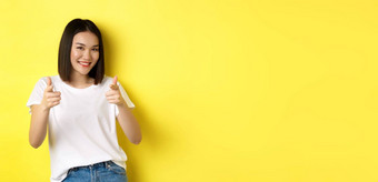 漂亮的年轻的亚洲女人白色t恤指出手指相机微笑赞扬选择恭喜站黄色的背景