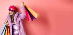 时髦的很酷的亚洲高级女人时尚衣服跳舞购物销售持有商店纸袋有趣的粉红色的背景