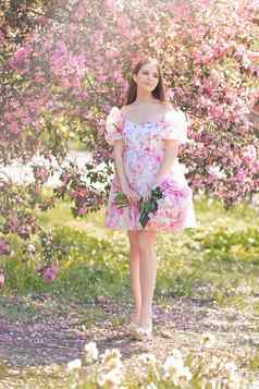 快乐浅黑肤色的女人衣服大花束牡丹站粉红色的盛开的苹果树