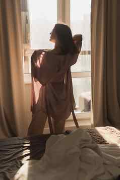 年轻的女人享受阳光明媚的早....卧室唤醒健康概念