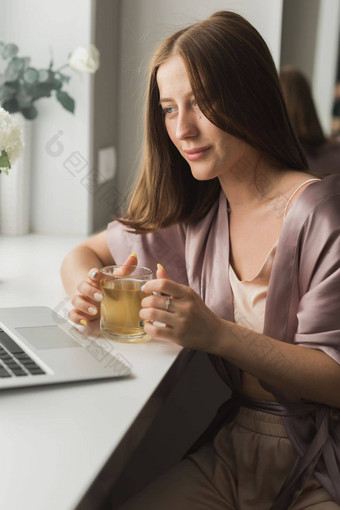 年轻的<strong>女人</strong>穿睡觉衣服工作移动PC电脑坐着生活房间<strong>喝茶</strong>社会网络工作首页概念