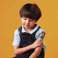 可爱的亚洲男孩持有手臂显示邦迪牌创可贴孩子穿石膏强迫疫苗伤心孩子注射橙色背景