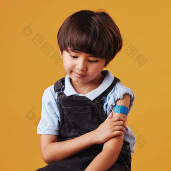 可爱的亚洲男孩持有手臂显示邦迪牌<strong>创可贴</strong>孩子穿石膏强迫疫苗伤心孩子注射橙色背景