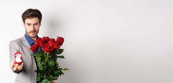 英俊的年轻的男人。使婚姻建议拉伸手订婚环持有红色的玫瑰结婚自信情人白色背景