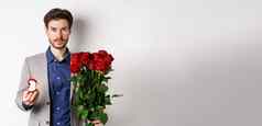 英俊的男人。西装使建议站红色的玫瑰花订婚井盒子使浪漫的惊喜白色背景