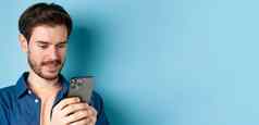 关闭肖像快乐年轻的男人。阅读移动斯雷恩网络智能手机站蓝色的背景