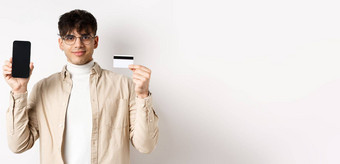 在线购物年轻的现代的家伙显示塑料信贷卡空智能<strong>手机</strong>屏幕<strong>演示</strong>账户站白色背景