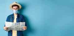 科维德流感大流行旅行概念年轻的男人。医疗面具阅读旅游地图搜索路线观光景点站蓝色的背景