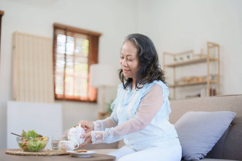 肖像上了年纪的亚洲女人喝健康的茶吃<strong>蔬菜</strong>沙拉<strong>零食</strong>