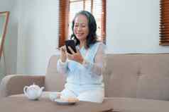 肖像上了年纪的亚洲女人持有移动电话吃零食喝茶
