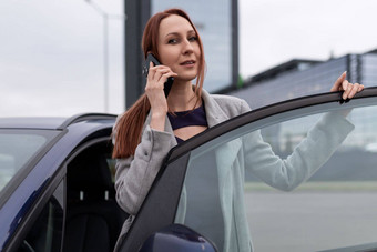 红发成人女商人会说话的移动电话车停车很多运行成功的业务概念