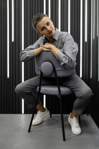 时尚的女<strong>人</strong>欧洲外观坐在椅子灰色的衬衫灰色的墙