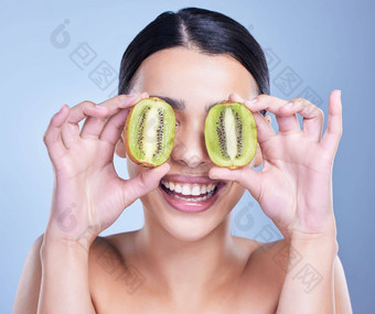 快乐微笑混合比赛女人持有猕猴桃水果拉美裔模型促进皮肤好处健康的饮食蓝色的Copyspace背景