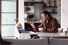 父亲穿浴绳勺子喂养希尔婴儿婴儿男孩孩子坐着高椅子餐厅表格厨房首页早....