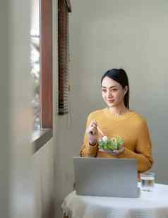 快乐亚洲女人吃健康的沙拉蔬菜混合移动PC生活房间工作首页