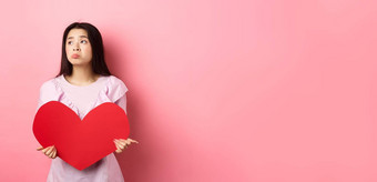 情人节概念孤独的十几岁的亚洲女孩做梦爱感觉伤心孤独的情人一天遗憾持有大红色的心粉红色的背景