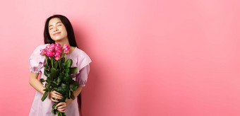 梦幻亚洲十几岁的女孩感觉浪漫的持有花做梦成像情人节一天日期穿可爱的衣服站粉红色的背景