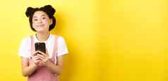 可爱的时尚的亚洲女孩移动电话穿魅力粉红色的化妆夏天衣服站黄色的背景