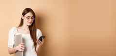 年轻的女孩眼镜聊天移动电话持有移动PC工作站米色背景