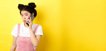 可爱的青少年女孩会说话的智能手机使愚蠢的撅嘴脸胆小相机站魅力化妆黄色的背景