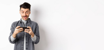 兴奋的家伙玩视频游戏移动电话集中脸利用智能手机屏幕持有手机水平白色背景