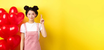 情人节一天概念时尚的十几岁的亚洲女孩浪漫的化妆持有手指交叉好运气使微笑站黄色的背景