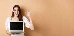 电子商务兴奋年轻的女人眼镜显示标志移动PC屏幕推荐互联网促销站米色背景