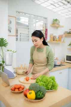 健康的食物饮食概念亚洲女人烹饪蔬菜沙拉晚餐切割成熟的西红柿木切董事会厨房首页