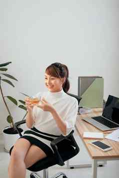 快乐的年轻的亚洲女人喝杯茶办公室