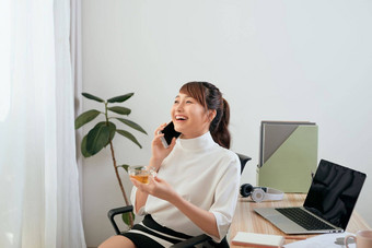 年轻的亚洲<strong>女人</strong>会说话的电话<strong>喝茶</strong>坐着办公室