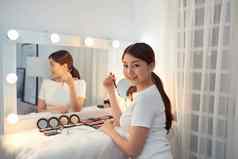美丽的亚洲女孩镜子应用化妆品刷