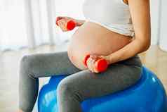 女人怀孕了妈妈。怀孕女锻炼体育运动健身肚子健康的孕妇母亲健康瑜伽年轻的哑铃重量
