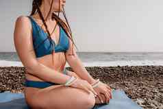 女人海瑜伽中间岁的女人辫子长发绺蓝色的泳装伸展运动普拉提瑜伽席海女健身瑜伽例程概念健康的生活方式