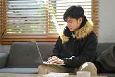 快乐的年轻的亚洲男人。浏览互联网网站购物在线移动PC舒适的生活房间