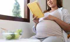 年轻的怀孕了女人坐着阅读书吃沙拉首页
