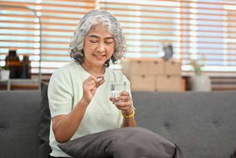 微笑成熟的女人持有药丸玻璃新鲜的水上了年纪的医疗保健药物治疗概念