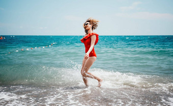 年轻的快乐女人走无忧无虑的<strong>海边</strong>快乐夫人<strong>红色</strong>的比基尼肖像美丽的年轻的女人放松微笑海滩海海洋假期假期旅行旅行