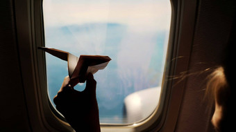 特写镜头轮廓孩子的手小纸飞机背景飞机窗口孩子坐着飞机窗口玩纸飞机飞行飞机