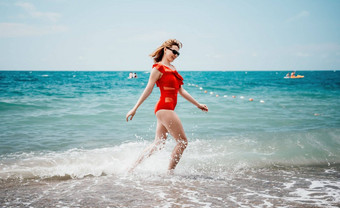 年轻的快乐女人走无忧无虑的海边快乐夫人红色的比基尼肖像美丽的年轻的女人放松微笑海滩海海洋假期假期旅行旅行