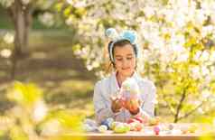 可爱的十几岁的女孩穿兔子耳朵持有复活节鸡蛋花园