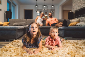 年轻的孩子们铺设毛茸茸的地毯看电影父母坐着<strong>沙发背景</strong>