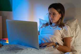 美丽的年轻的女孩坐着床上晚上工作移动PC中间晚上