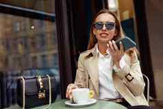 女人穿眼镜记录音频消息移动电话喝咖啡咖啡馆阳台