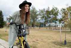 快乐的年轻的女人灰色的外套黑色的他游乐设施自行车微笑