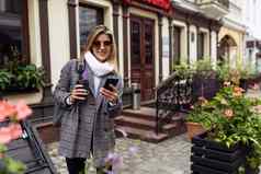 成熟的女人旅游太阳镜智能手机玻璃咖啡走城市